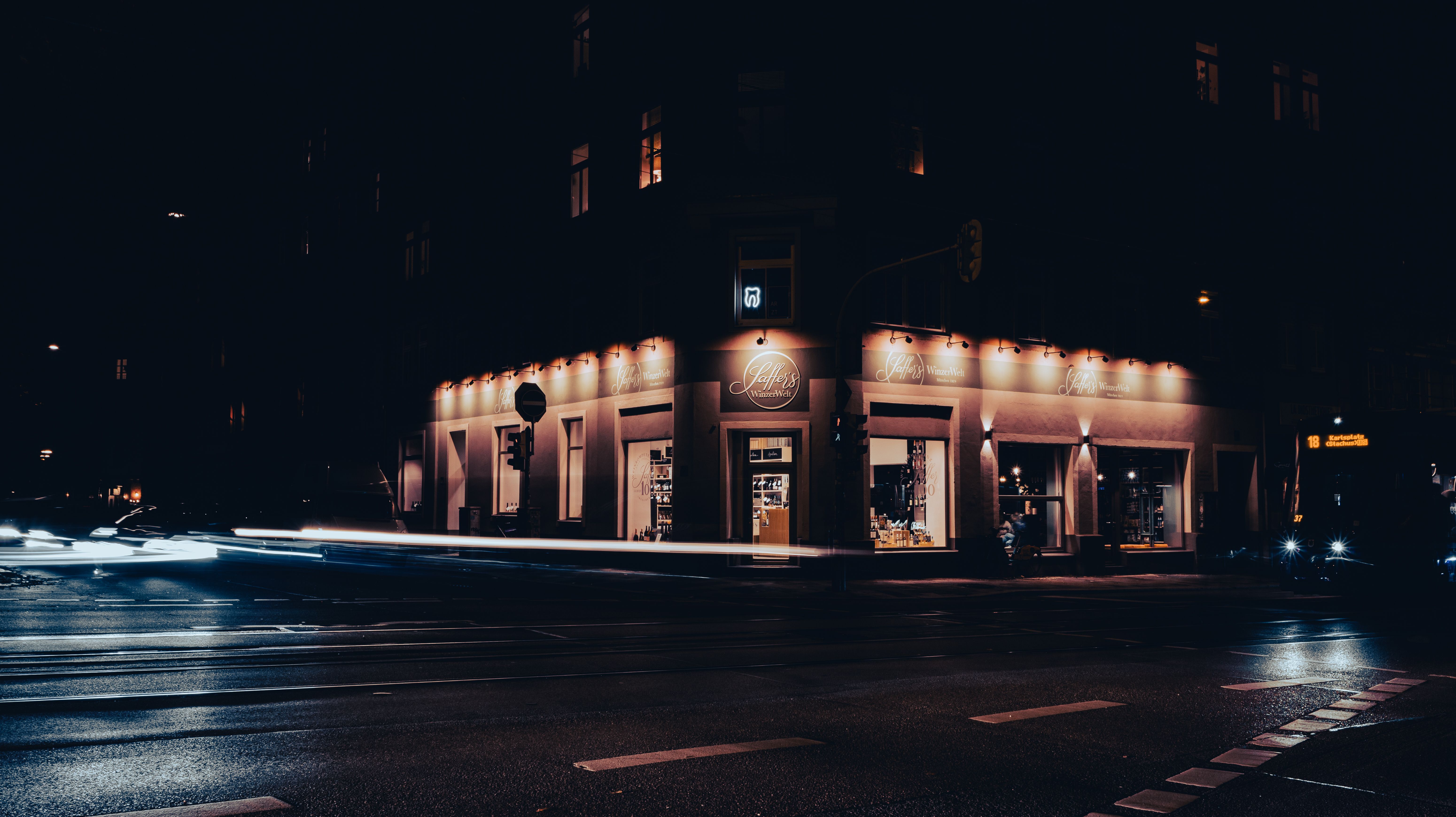 Munich street corner at night with illuminated storefronts and urban light trails.